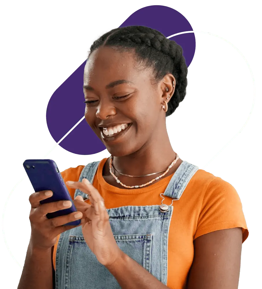 Mulher jovem olhando para um celular e sorrindo. Ela está usando uma camiseta na cor laranja e e um macacão jeans